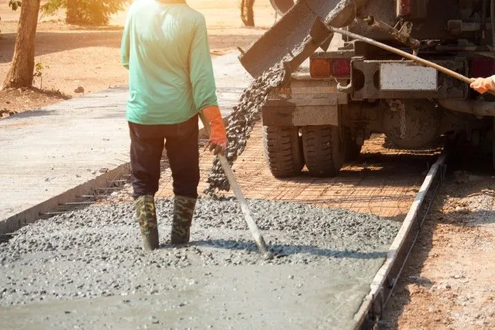 A worker in rubber boots levels wet concrete pouring from a truck on a roadway in Benton, Arkansas
