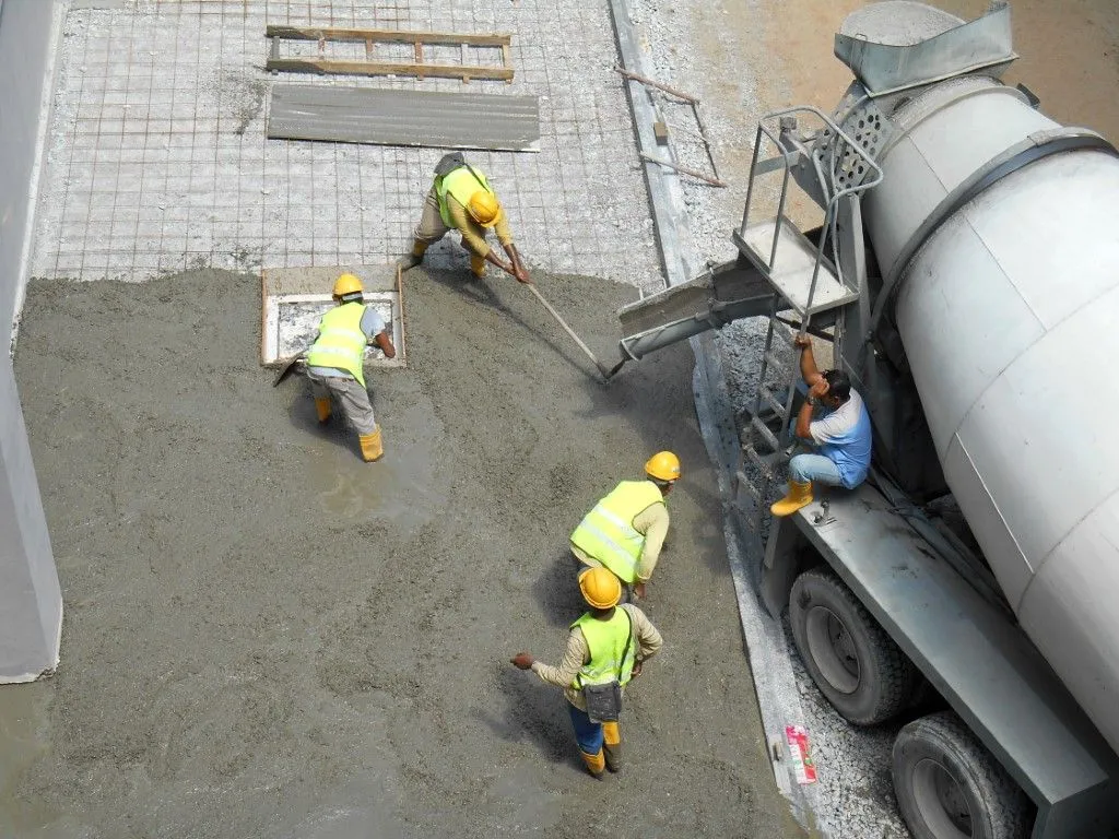Construction workers pouring concrete from a truck to a prepared area, wearing yellow vests and helmets in Benton, Arkansas